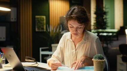 Manager researching numbers and finance figures in a dark office after hours, documenting updates and organizing the agenda for business presentation. Setting targets at night. Camera B.