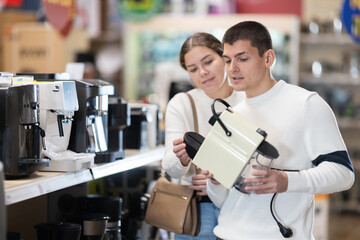 Young couple man and woman choosing electric coffee machine in home appliance store