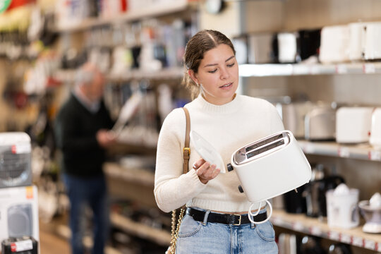 Young woman buyer chooses electric toaster in home appliance store