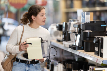 Young woman buyer chooses electric coffee machine in home appliance store