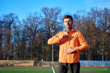 Man standing on outdoor sports field adjusting jacket during warm up exercise