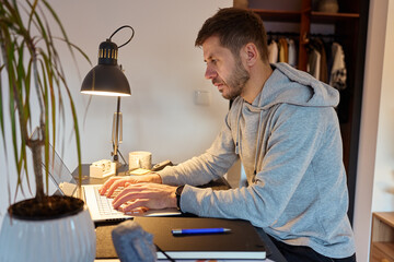 Man sitting at desk using laptop computer under desk lamp in home interior