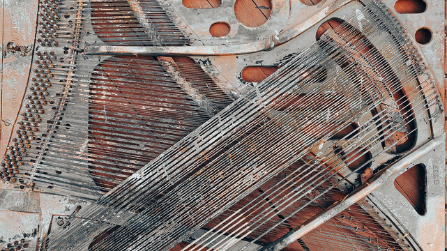 Rusty metal piano strings are stretched across a weathered frame creating an abstract pattern with bolts and holes on aged wood in a close up textured view