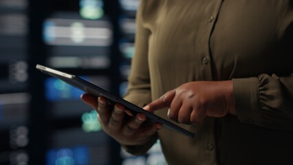 Close up shot of admin working in data center using tablet to optimize network mainframes. IT employee in server farm diagnosing and resolving hardware glitches using device
