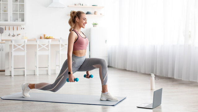 Satisfied european pretty young blonde fitness woman do exercises with dumbbells and watch online workout video on laptop at home, panorama. Social distance, sports and lesson remotely with device