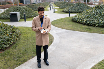 Young professional man standing in park enjoying a take away lunch during a casual outdoor work break