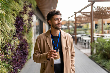 Employee having coffee break outdoors at an eco-friendly office campus, walking on pathway next to a green wall