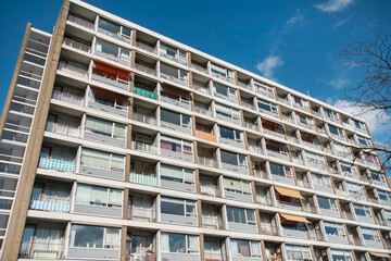 Multi-story residential apartment block with white balconies and varied window treatments under blue sky