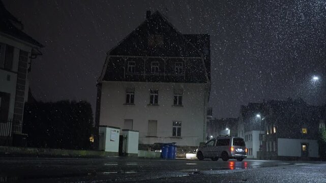 Vehicle Rests Under Glowing Lamppost, Small Car Pauses Beneath Streetlight Amidst Snow And Shining Reflections, Parked Vehicle Beneath Streetlamp Casts Red Reflections Over Damp Road Surface Near Home