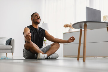 Online Yoga Lesson. Happy Black Man Meditating In Front Of Laptop Sitting In Lotus Position Doing...