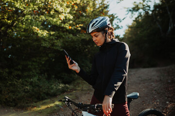 Woman with a helmet using a smartphone for navigation while cycling outdoors