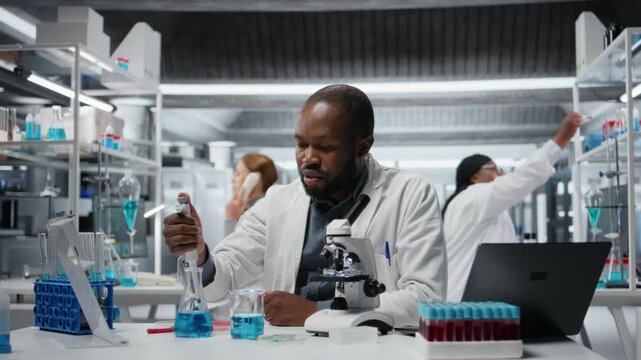 Assay development specialist pipetting reactant into blue solution for purity analysis. Man in research facility lab adding liquid agent to test tube to observe chemical reaction properties, camera A