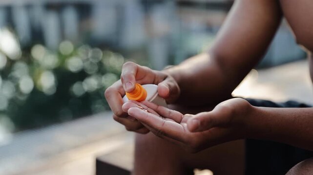 Person applying sunscreen lotion to hand, protecting skin from sun during summer vacation or outdoor activity. Black young man putting sunscreen on his body at resort pool