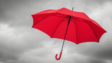 A single red umbrella its fabric billowing dramatically in the wind making a bold statement against a grey dreary day.