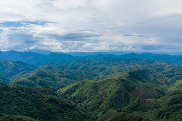 Sweeping panorama of undulating green hills and distant blue ridges beneath a vast sky filled with layered clouds in the Laotian countryside between Phonsavan and Phou Khoun. The landscape showcases