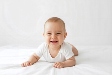 Smiling baby boy lying on a white bed, showcasing joy and innocence in a bright setting.