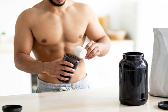 Closeup of young man with bare torso making protein shake to build up muscles ot lose weight at kitchen. Unrecognizable bodybuilder preparing cocktail, keeping diet, following nutritional meal plan