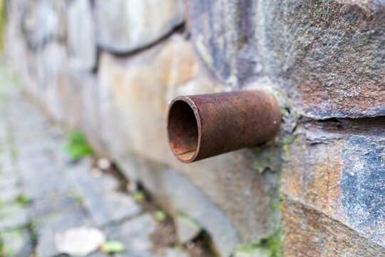 A rusty pipe is sticking out of a wall. The pipe is bent and has a hole in it