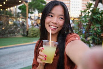 Happy young woman taking a selfie while drinking lemonade at a summer festival