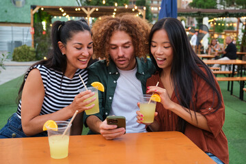 Three friends are enjoying cocktails and watching social media content during a summer party at a street food market