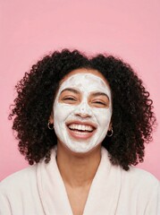 Smiling Black woman with curly hair enjoying a facial mask against a pink background.