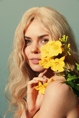 Bright and vibrant portrait of a young woman with wavy blonde hair holding yellow flowers against a soft blue background, radiating positivity and warmth.