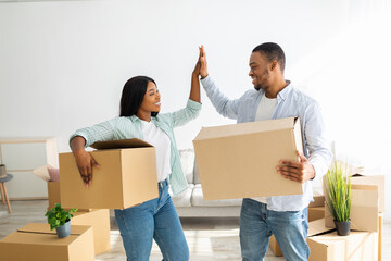 Packed and ready to move into new house. Black spouses giving high-five, holding cardboard boxes...