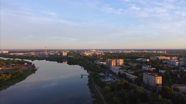 Drone flies along the Volga River at sunrise in Tver. The calm water reflects the soft morning sky, and the city is visible on both sides of the river.