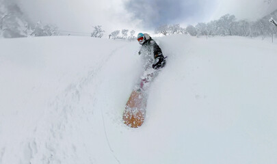 SELFIE: Woman snowboards through deep powder in Niseko, Japan. Soft snow sprays through the air as she carves down an open slope. Famous snow of Hokkaido and the thrill of winter freeride adventures. © helivideo