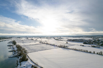 Aerial view of frozen over covered in snow floodplains flood land area opposite Dutch tower town Zutphen in the Netherlands De Hoven neighbourhood in the background. Graphic painterly picturesque wint