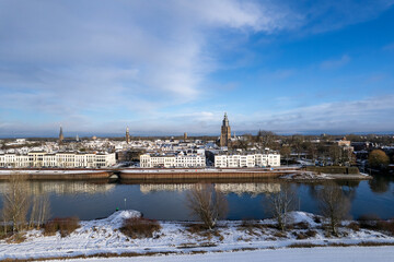 Countenance aerial view of medieval Hanseatic Dutch tower town Zutphen in the Netherlands covered in snow with historic heritage buildings and river IJssel passing by in the foreground