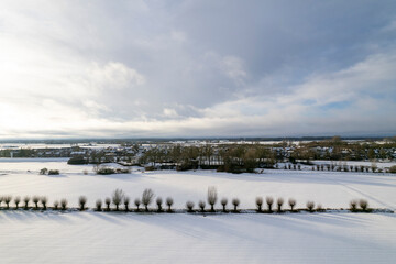 Frozen over covered in snow floodplains flood land area opposite Dutch tower town Zutphen in the Netherlands De Hoven neighbourhood in the background. Graphic painterly picturesque winter wonderland a
