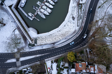 Cars on meandering road along recreational port with boats. Graphic winter landscape aerial top down Dutch tower town Zutphen in The Netherlands covered in snow