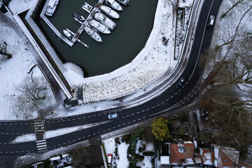 Meandering road and recreational port with boats. Graphic winter landscape. Aerial top down Dutch tower town Zutphen in The Netherlands covered in snow