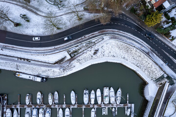 Aerial top down Dutch tower town Zutphen in The Netherlands covered in snow with meandering road and recreational port with boats. Graphic winter landscape