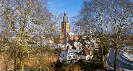 Picturesque winter wonderland medieval Hanseatic Dutch tower town Zutphen in the Netherlands covered in snow with historic heritage Walburgiskerk church seen from above through winter barren trees