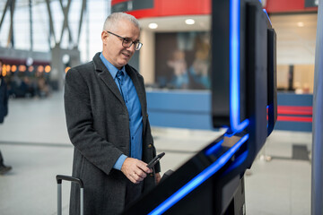 Mature man using smartphone at airport check-in kiosk