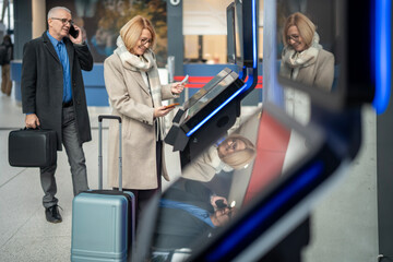 Senior couple using self-service kiosk at airport