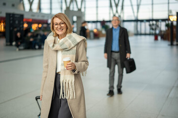 Obraz premium Smiling mature woman traveling through modern airport terminal