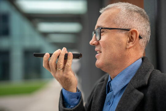 Mature man speaking into smartphone using voice recognition technology - Powered by Adobe