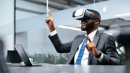A man sits at a desk in an office, wearing a virtual reality headset while interacting with a digital environment. His hands are raised, suggesting engagement with a virtual activity.