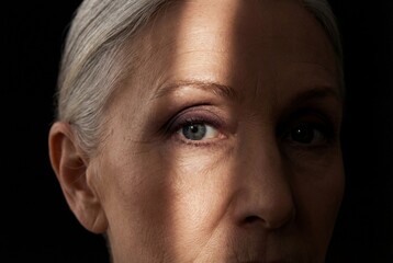 Fototapeta premium Close up of senior woman face with dramatic lighting illuminating blue eye and wrinkled skin texture