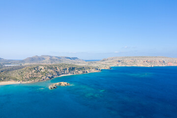 Obraz premium Expansive aerial view of a rugged coastal headland jutting into deep blue Mediterranean waters near Vai beach, Crete. The scene features sunlit cliffs, clear turquoise shallows, and a bright sky for a