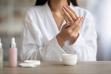 Unrecognizable asian woman rubbing her hands, using nourishing cream at home. Young lady in...