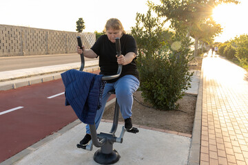 Determined woman exercising on outdoor fitness bike at sunset