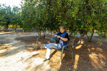 Woman relaxing in park opening her bag on bench