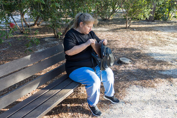 Woman searching backpack on park bench outdoors