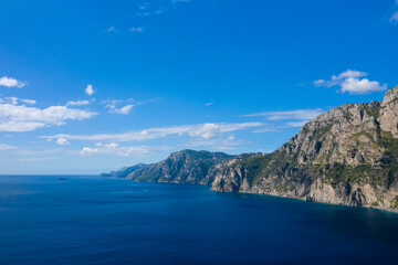 Obraz premium Expansive view of rugged limestone cliffs meeting deep blue Mediterranean waters under a clear sky. Sunlight highlights the natural textures and dramatic coastline typical of the Italian countryside.
