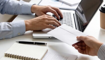 Hands exchanging an envelope over a desk; one person types on a laptop while working with papers and coffee.