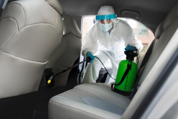Worker in hazmat suit with chemical alcohol spray cleaning inside car to disinfect and decontaminate covid-19 by specialist cleaner wearing personal protective equipment PPE. New normal, hygiene